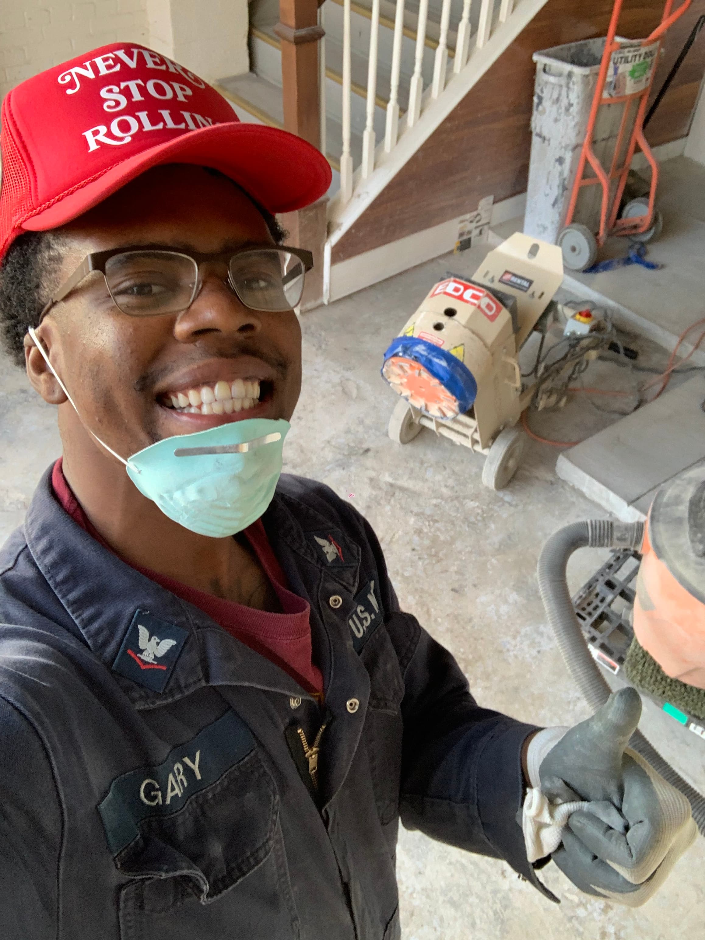 Smiling man in red cap and navy uniform gives a thumbs up at a construction site.