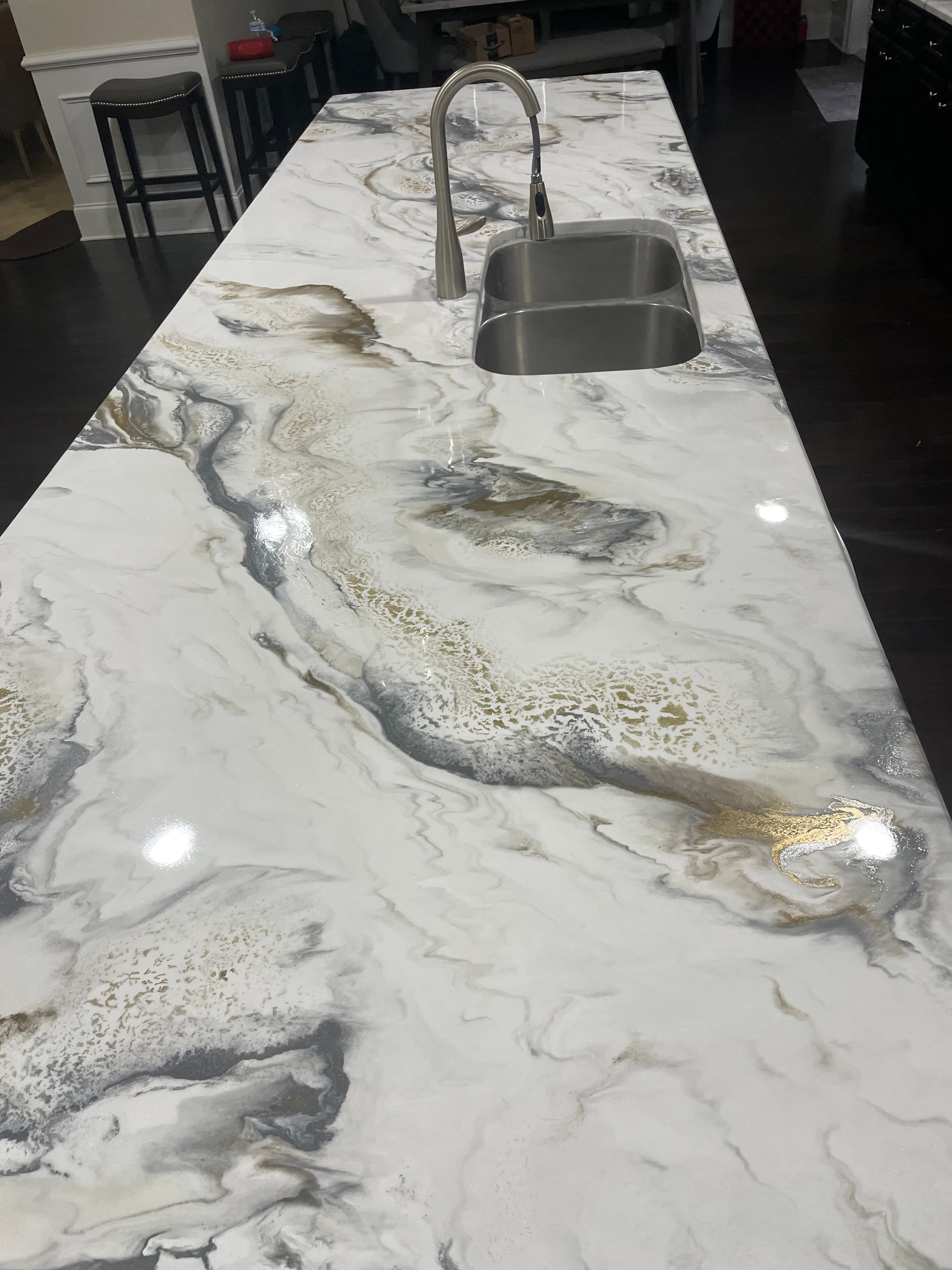 Glossy white countertop with grey and gold marble patterns and a stainless steel sink.